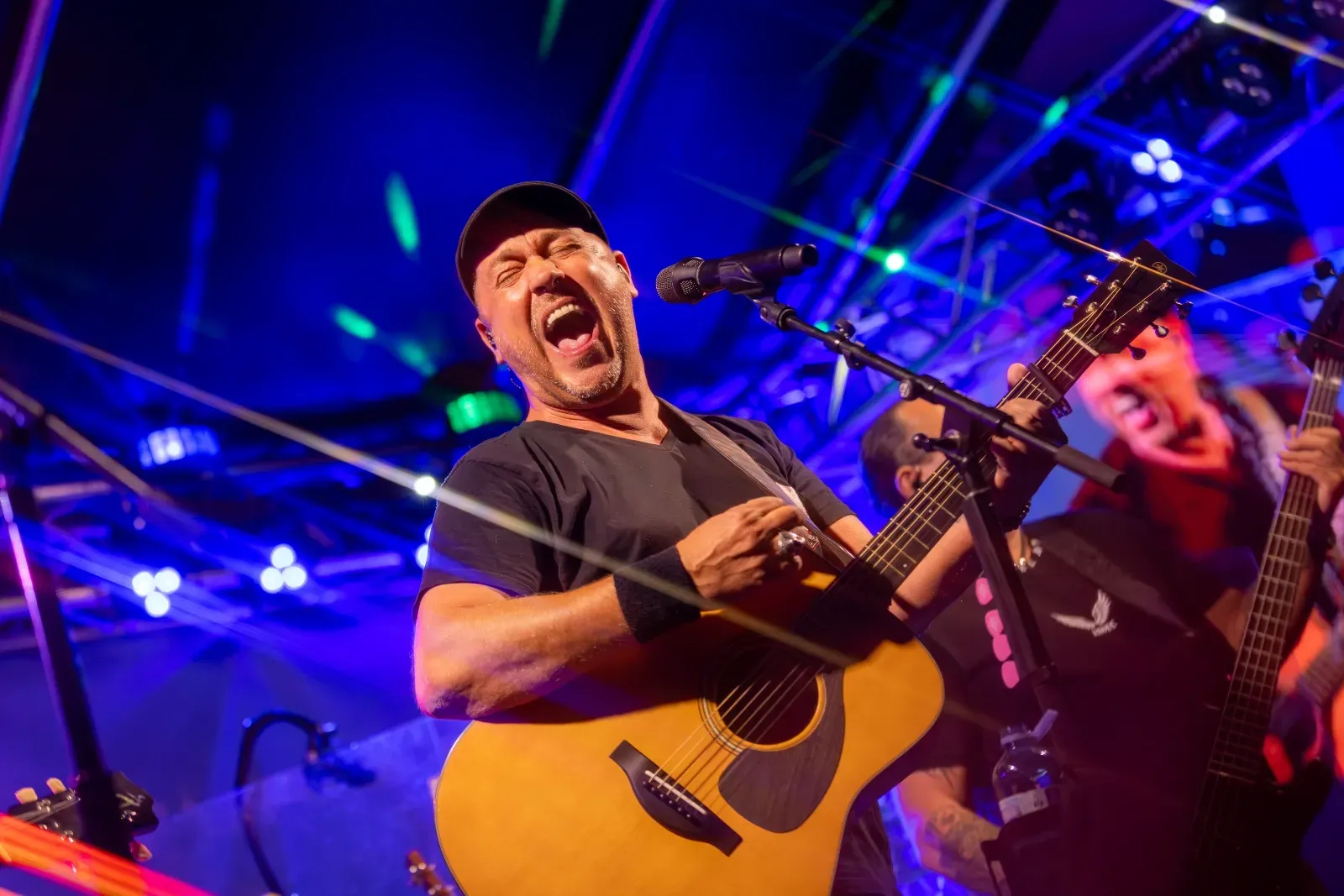 Gitarrist singt mit voller Kraft ins Mikrofon, dahinter die Band