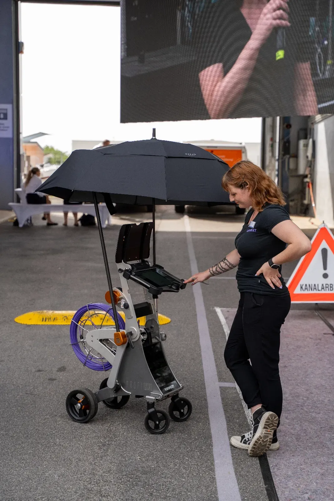 Eine Mitarbeiterin präsentiert einen fahrbaren Inspektionswagen mit aufgespanntem Schirm