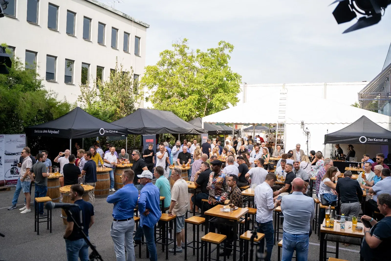 Volle Terrasse mit Stehtischen, Fassbar und Pavillons am frühen Abend