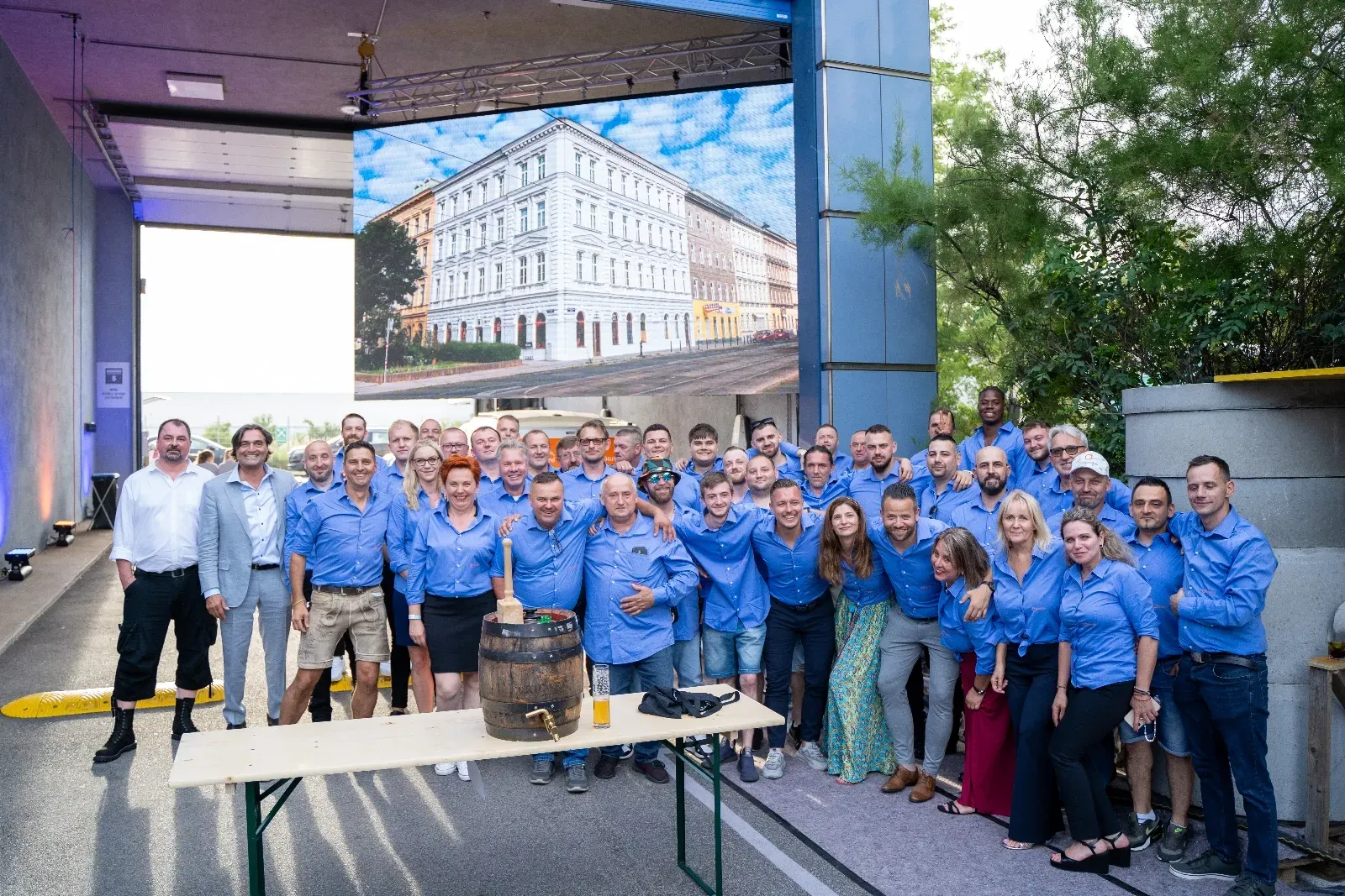 Gruppenbild des Teams in blauen Hemden vor der LED-Wand, davor das Bierfass