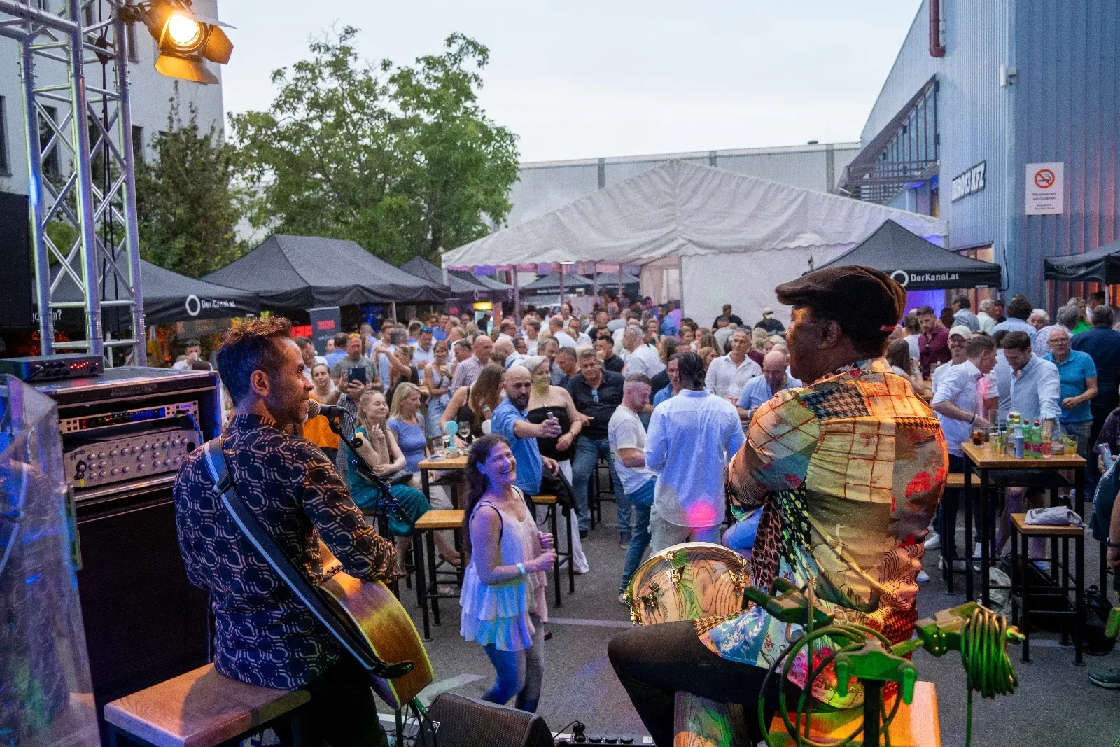Zwei Musiker auf der Bühne, davor das Publikum im Abendlicht